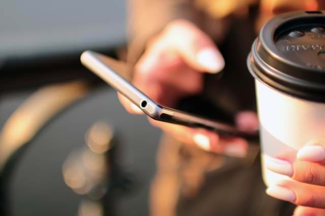 Person holding a cell phone with coffee