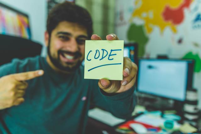 Man holding up post-it with Code written on it