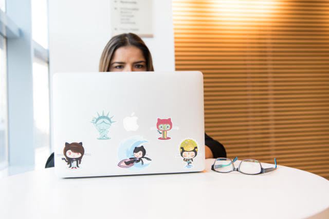 Woman hiding behind a laptop with Github stickers
