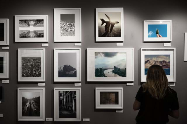 Woman sitting down looking at multiple works of art on a wall.