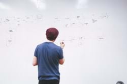 Man staring at a whiteboard with flowchart diagrams.